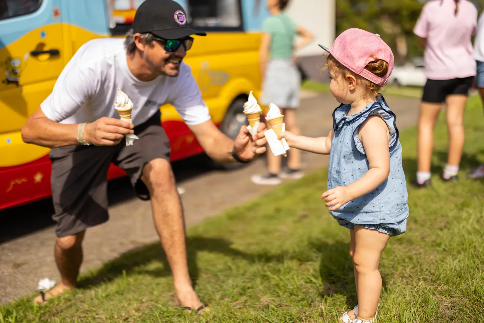 A dad and toddler taking soft serve cones from the Andersons' Ices ice cream van at a Gold Coast event